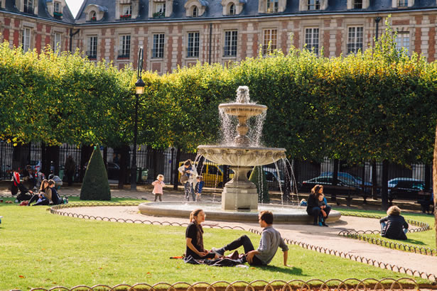 People sitting on the lawn in the middle of the Place des Vosges.