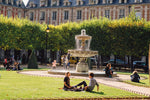 Load image into Gallery viewer, People sitting on the lawn in the middle of the Place des Vosges.
