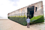 Load image into Gallery viewer, A man stands in front of a &quot;Mulberry&quot; at the artificial harbor at Arromanches.
