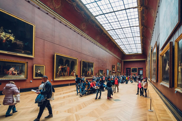 Tourists admiring some renaissance era paintings in the Louvre museum.